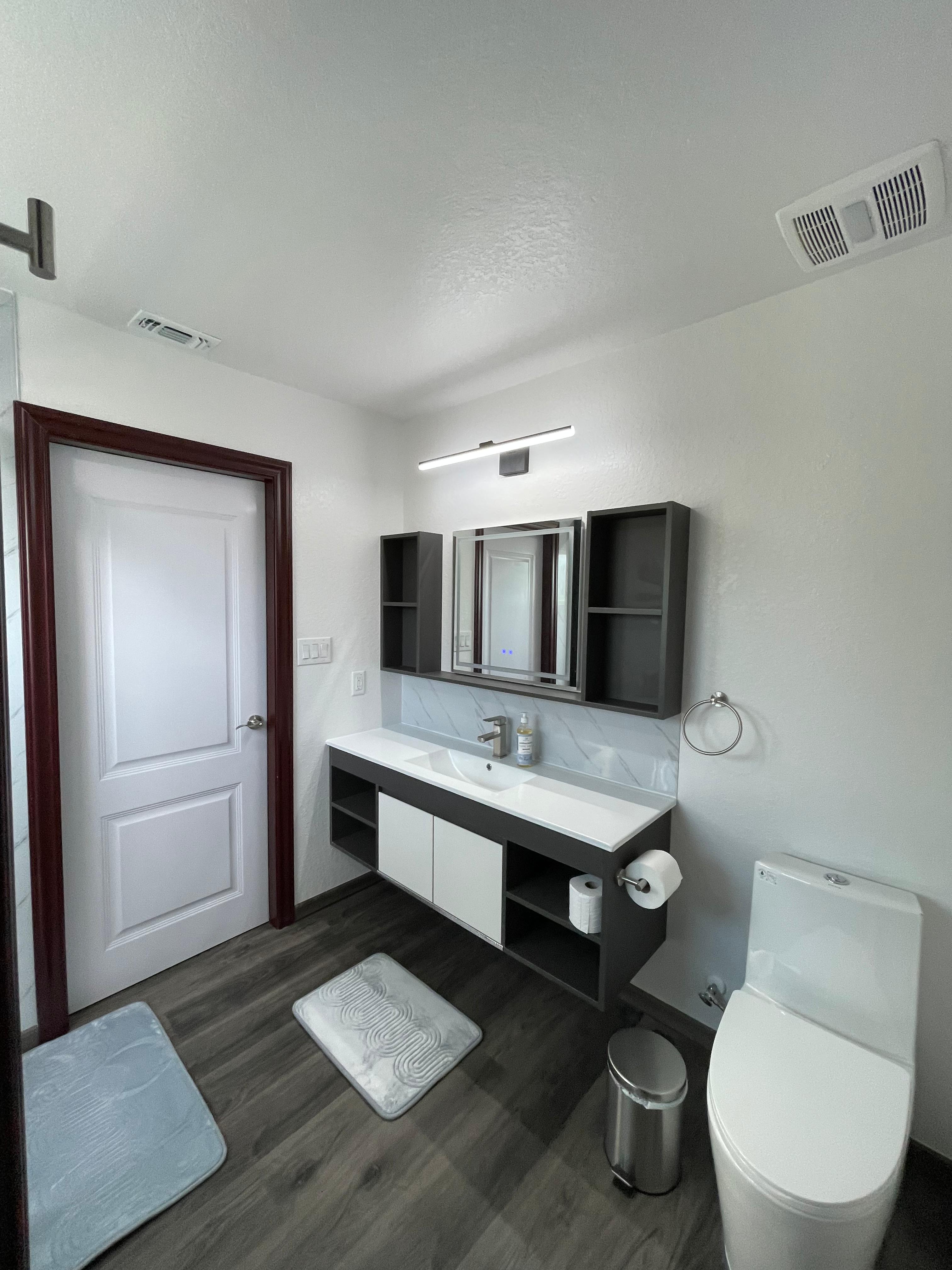 Apartment bathroom with double vanity, toilet, mirrors, and white shower door