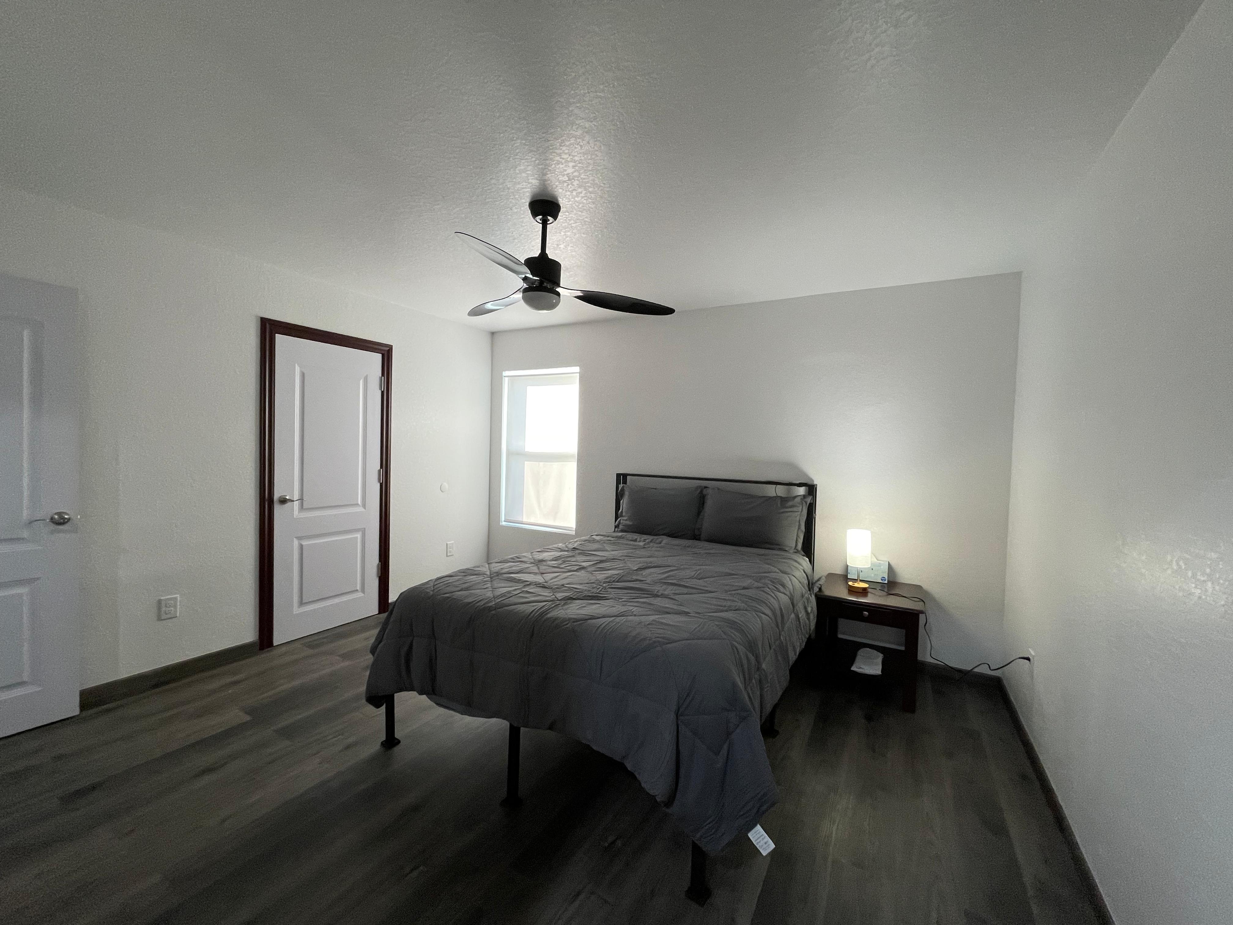 Apartment bedroom with dark flooring, ceiling fan, bed, side table, and window