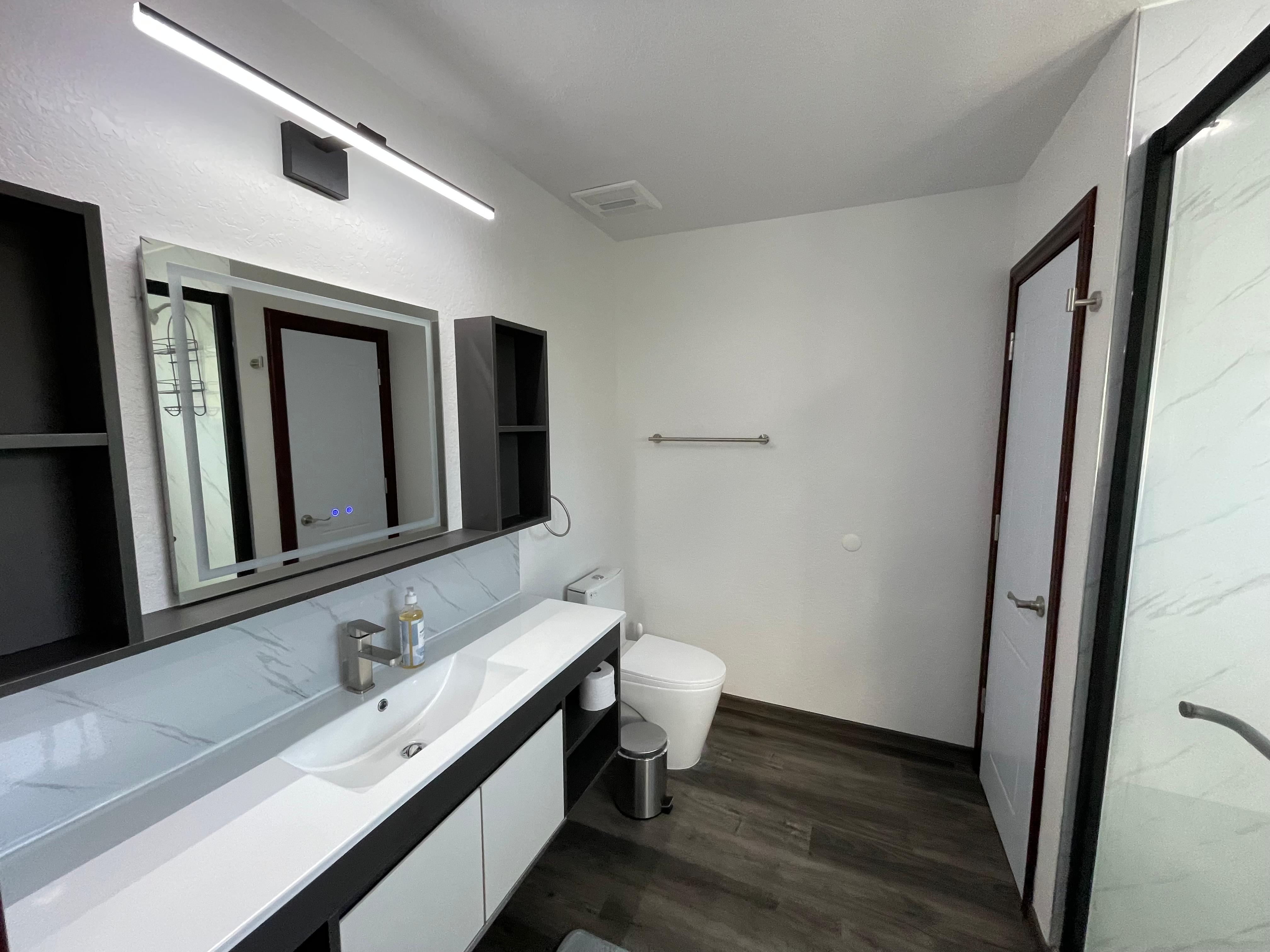 Apartment bathroom with double vanity, large mirrors, toilet, and walk-in shower door