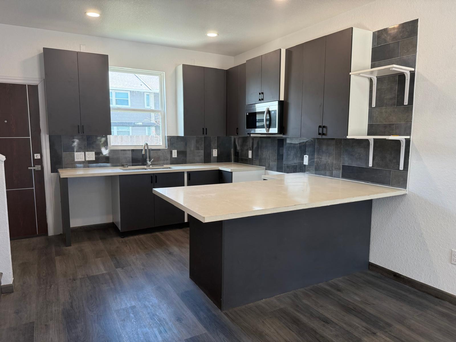 Apartment kitchen with dark cabinets, island, stainless appliances, and bright window