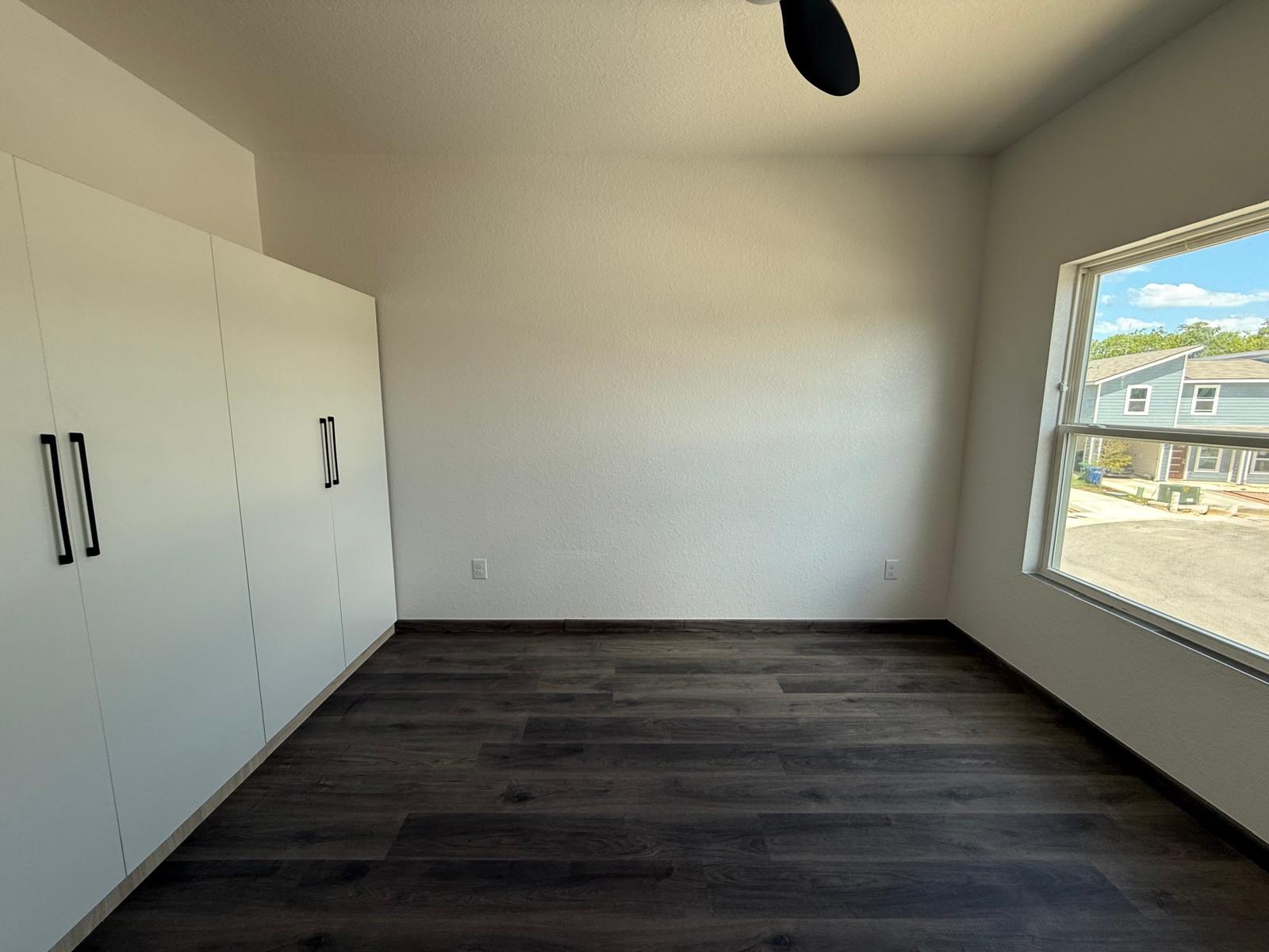 Empty apartment bedroom with built-in white wardrobe cabinets and large window