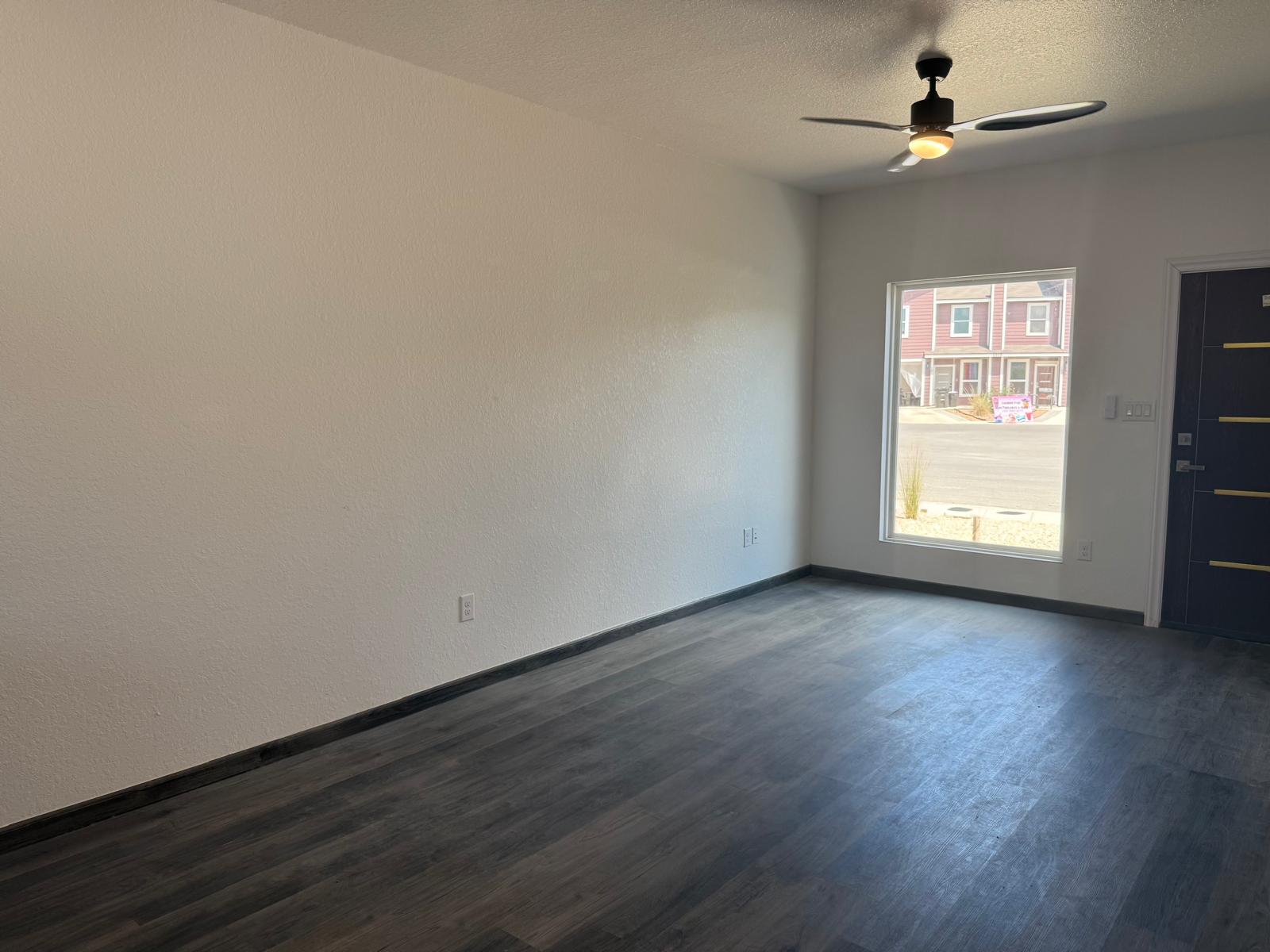 Unfurnished apartment room with dark flooring, black ceiling fan, window, and entry door